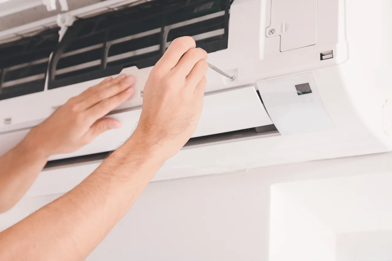 Hands cleaning an open wall-mounted air conditioner filter